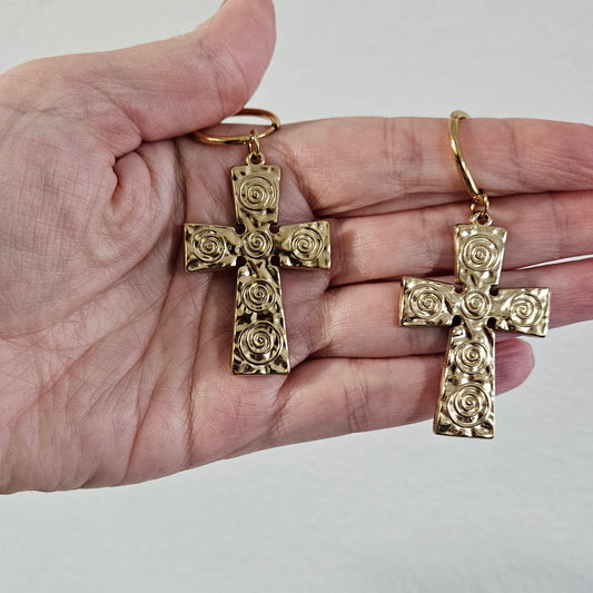 Gold cross pendants held in a hand against a plain background